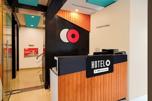 A hotel reception desk with a wooden finish and a sign indicating it is serviced by OYO.