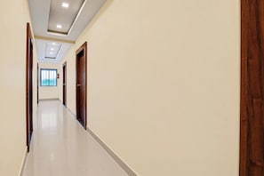 A hallway with a tiled floor, wooden doors, and a fire extinguisher on the wall. - Hotel O Khadakwasla Lake (Pune)