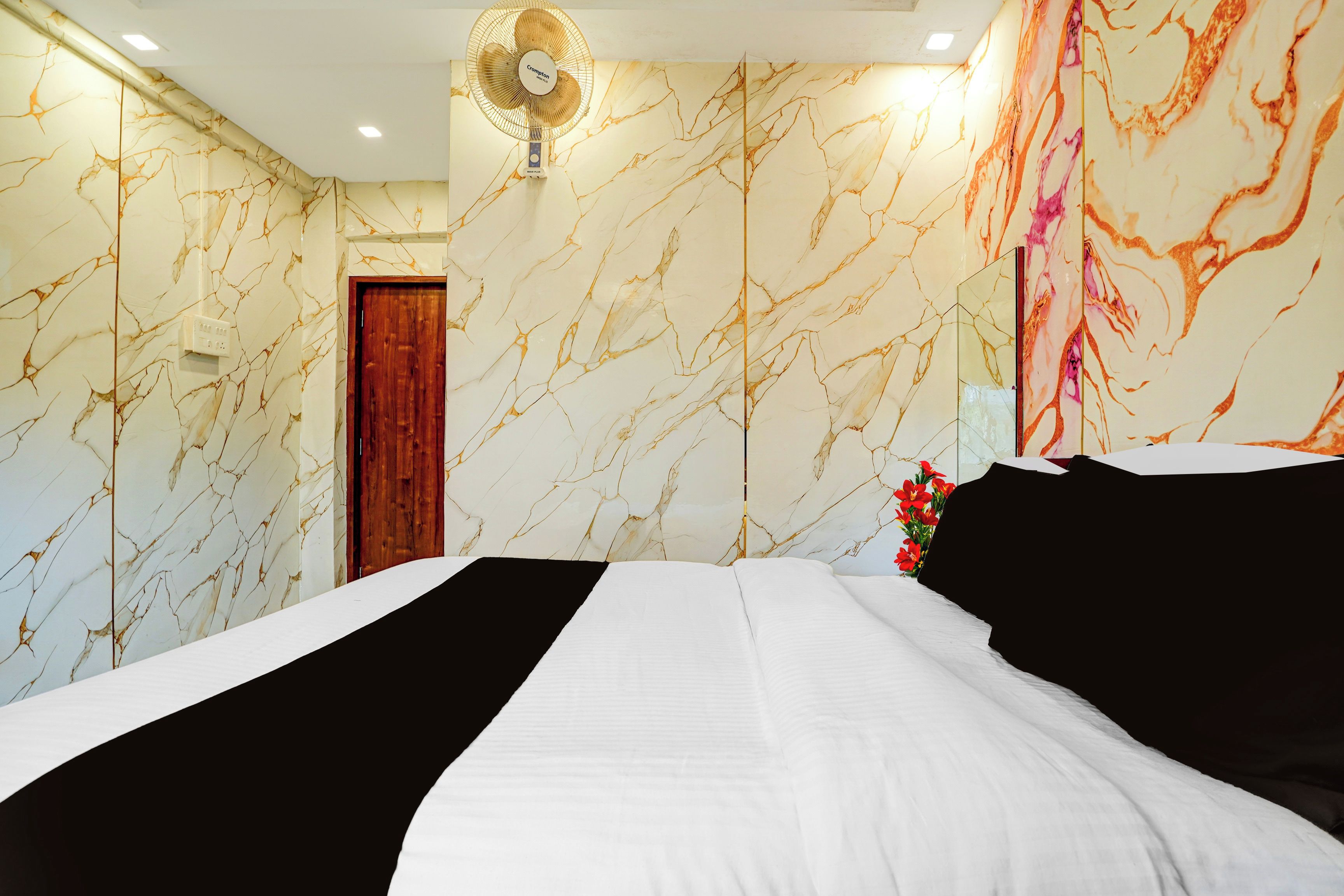 Quarto de hotel com cama, ventoinha, porta de madeira e parede com padrão marmorizado.