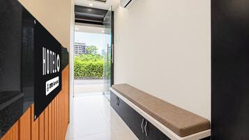 Zona de recepción de un hotel con un banco, un cartel que indica 'HOTEL' y 'YO-Serviced', y vista al exterior.