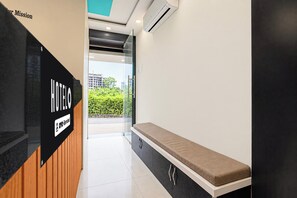 Zona de recepción de un hotel con un banco, un cartel que indica 'HOTEL' y 'YO-Serviced', y vista al exterior.