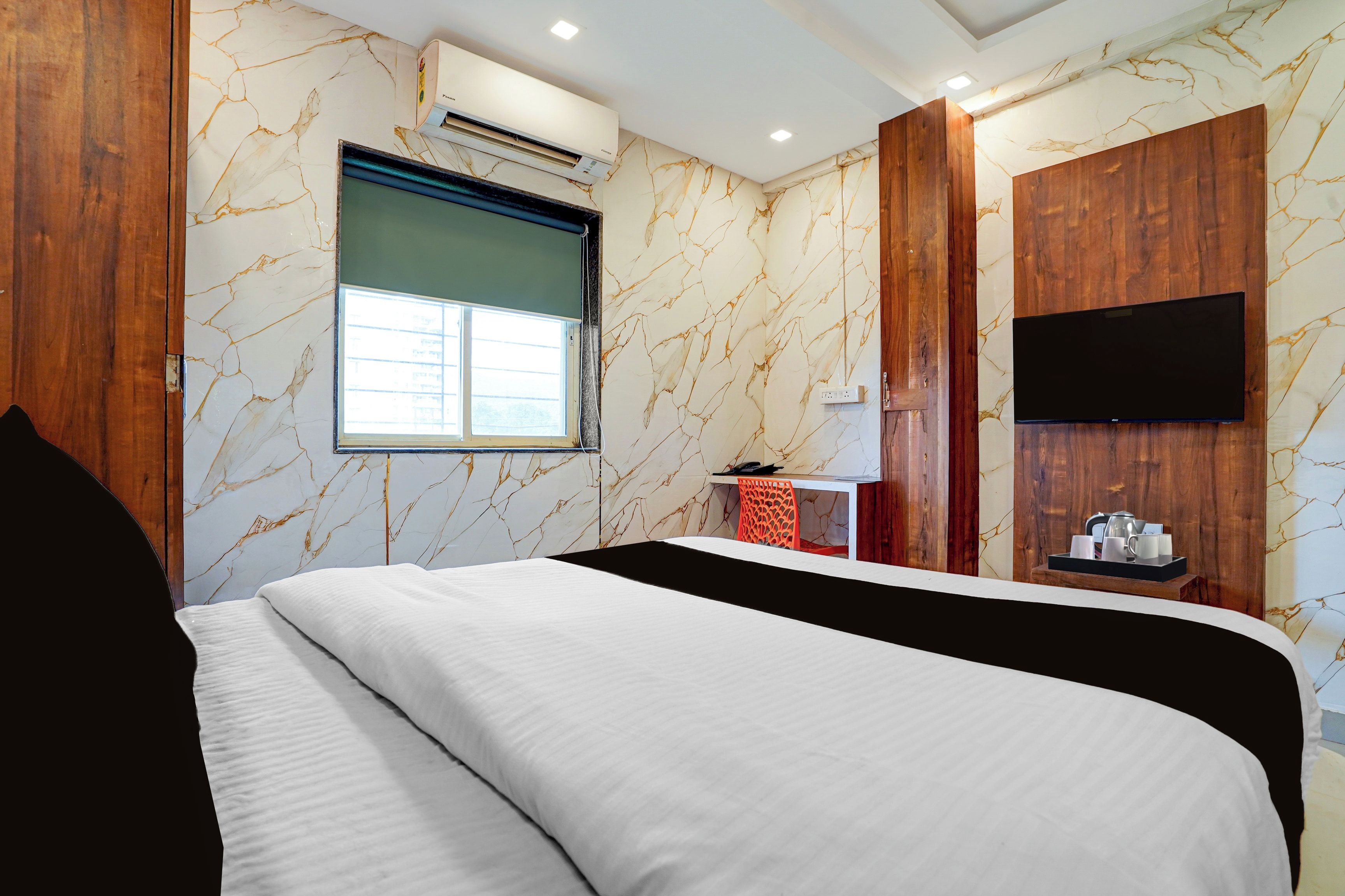 A hotel room with a bed, a TV mounted on the wall, and a window with a view.