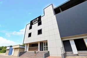 A modern hotel building with a prominent sign, a staircase leading to the entrance, and a clear sky in the background.