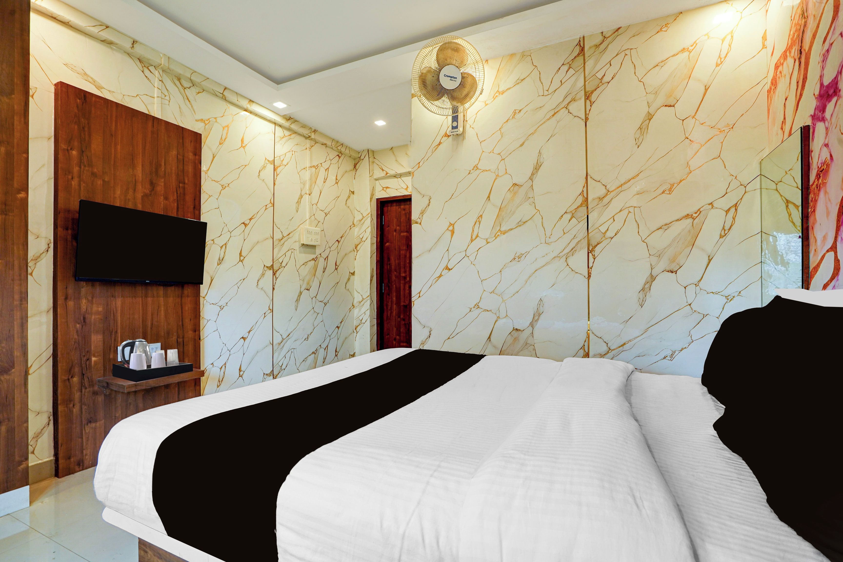 Habitación de hotel con cama, armario de madera, televisor de pantalla plana y pared con diseño de mármol.