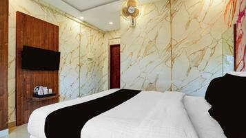 Habitación de hotel con cama, armario de madera, televisor de pantalla plana y pared con diseño de mármol.