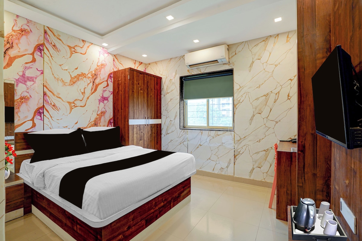 A hotel room with a bed, wooden wardrobe, marble-patterned walls, an air conditioning unit, a television, and a tray with a kettle and cups.