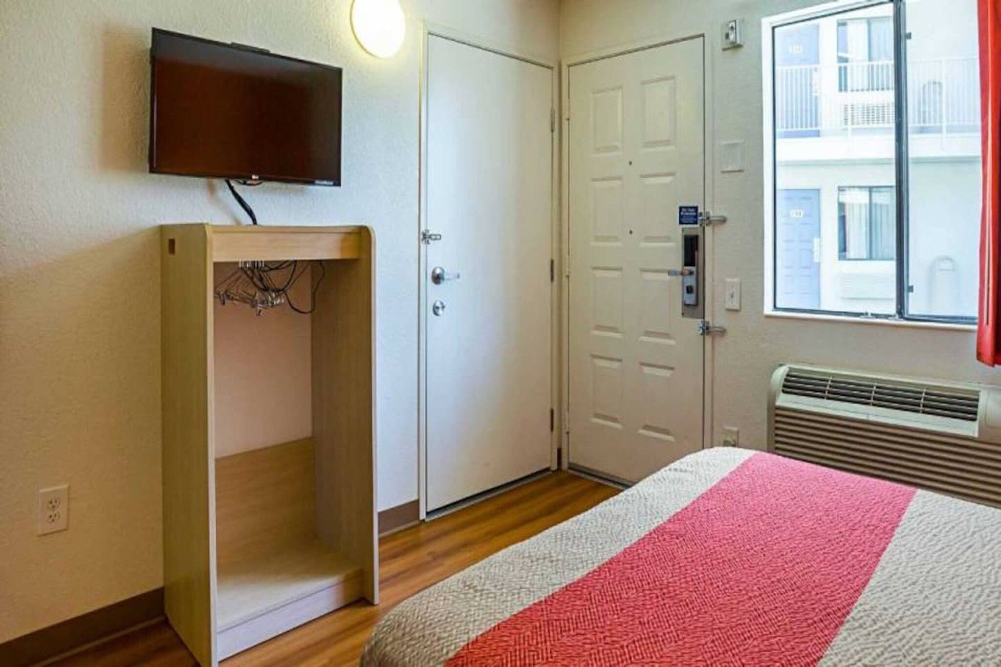 Une chambre d’hôtel comprenant un lit, un téléviseur fixé au mur, une armoire et une fenêtre donnant sur des immeubles.