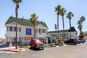 A motel with a '6' sign, multiple parking spaces, and palm trees. - 1 Queen Bed | Hearing Accessible Micfridge (Yuma AZ)