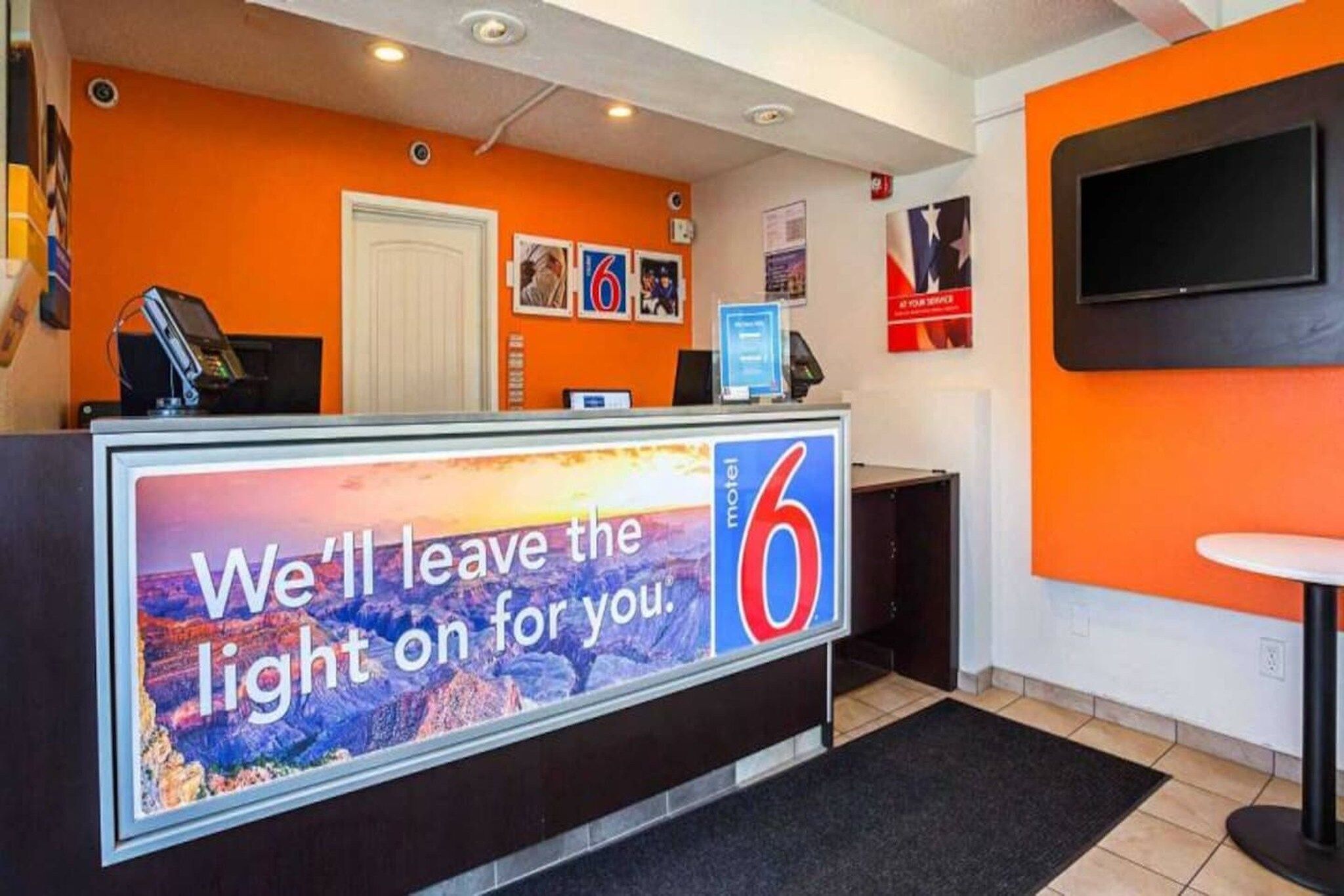 Un comptoir d’accueil d’hôtel avec une grande enseigne publicitaire, un ordinateur et un téléviseur fixé au mur.