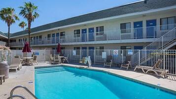 A hotel with a swimming pool, outdoor seating, and a two-story building.