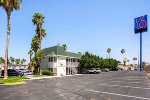 A motel with a parking lot, a building with a green roof, and palm trees. - 1 Full Bed | ADA/Tub/Micfridge (Yuma AZ)