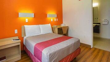 A hotel room with a bed, bedside table, and a desk with a chair.