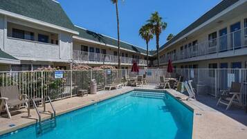 A hotel with a swimming pool, sun loungers, and a fenced area.