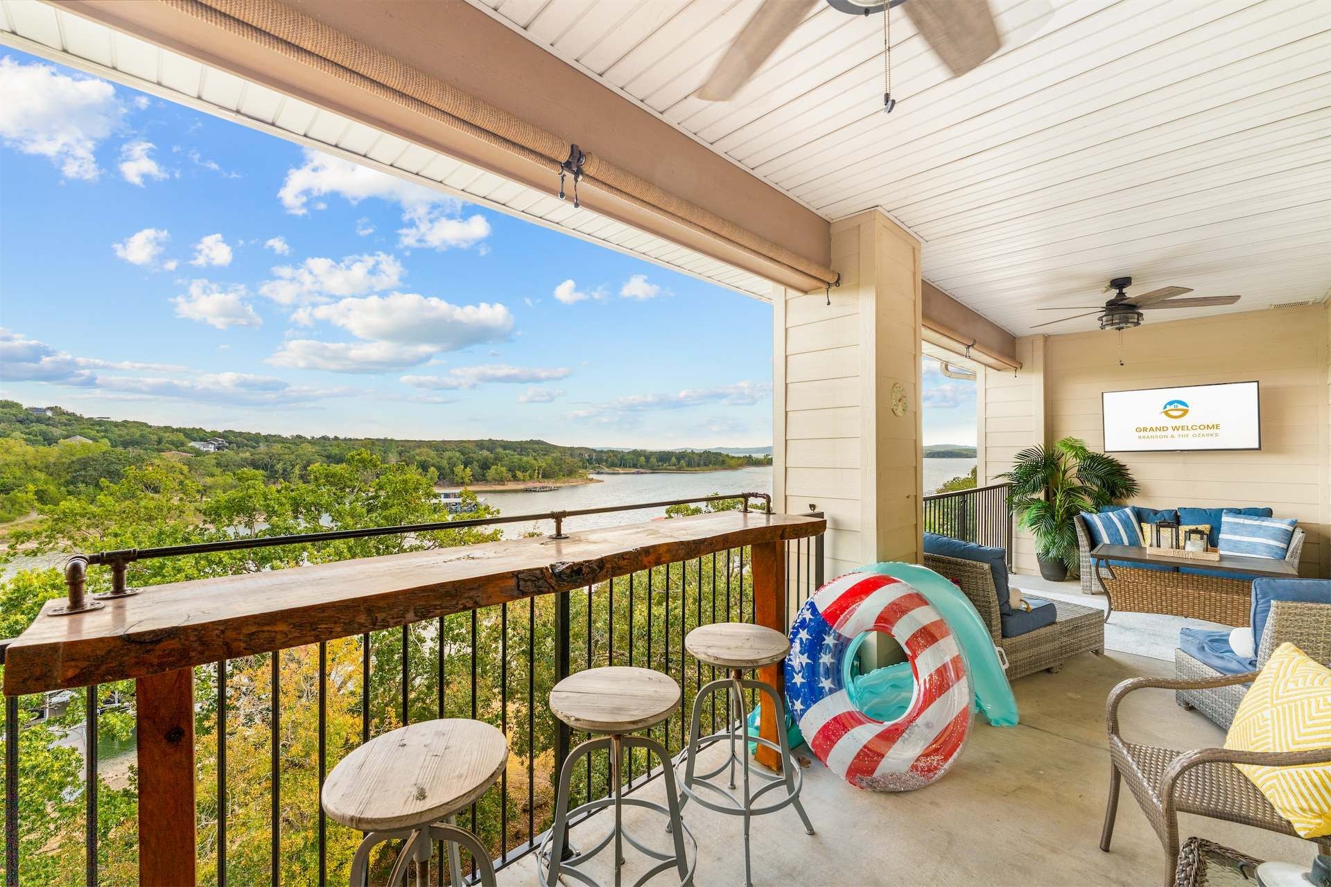 A balcony with a view of a river, a wicker sofa, and a table with stools.