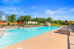 A clear swimming pool with lounge chairs and umbrellas, surrounded by a fence and trees. - Lakeside Leisure Lake Views (Branson)