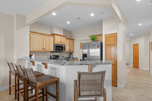 A modern kitchen with wooden cabinets, a stainless steel refrigerator, and a granite countertop. - Lakeside Leisure Lake Views (Branson)