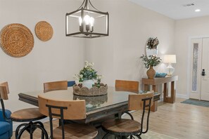 A dining area with a glass table surrounded by wooden chairs, a hanging light fixture, woven wall decorations, and a small side table with a lamp and decorative items. - Lakeside Leisure Lake Views (Branson)