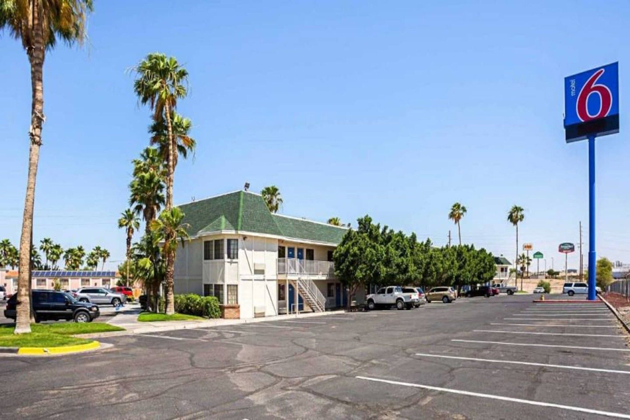 Un motel avec un parking, un bâtiment doté d’un toit végétalisé et des palmiers.