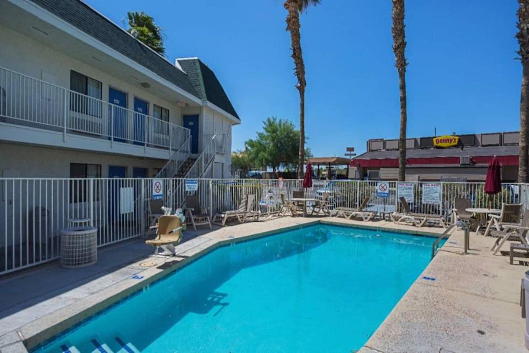 A swimming pool with lounge chairs, a building with balconies, and palm trees.