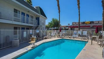 A swimming pool with lounge chairs, a building with balconies, and palm trees.