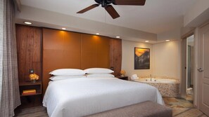 Une chambre d’hôtel avec un grand lit, une salle de bain séparée avec une baignoire et un ventilateur de plafond.