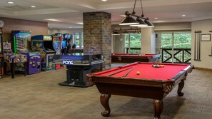 Une table de billard, des jeux d’arcade et une table de billard dans une pièce donnant sur un espace verdoyant.