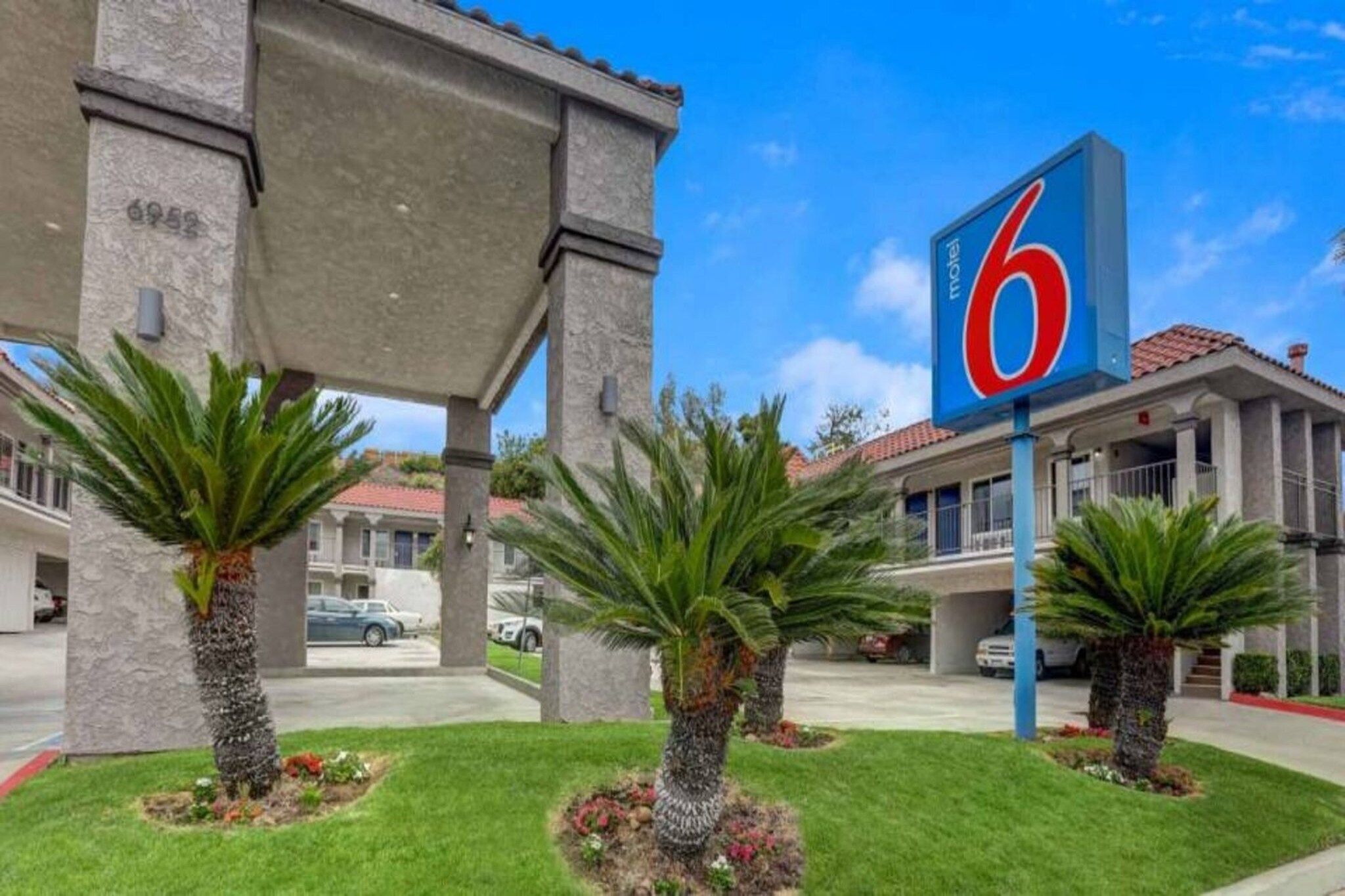 A motel with a large '6' sign, palm trees, and a covered parking area.
