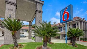 A motel with a large '6' sign, palm trees, and a covered parking area.