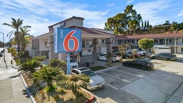 A motel with a prominent '6' sign, a parking lot with several cars, and a building with a red-tiled roof.