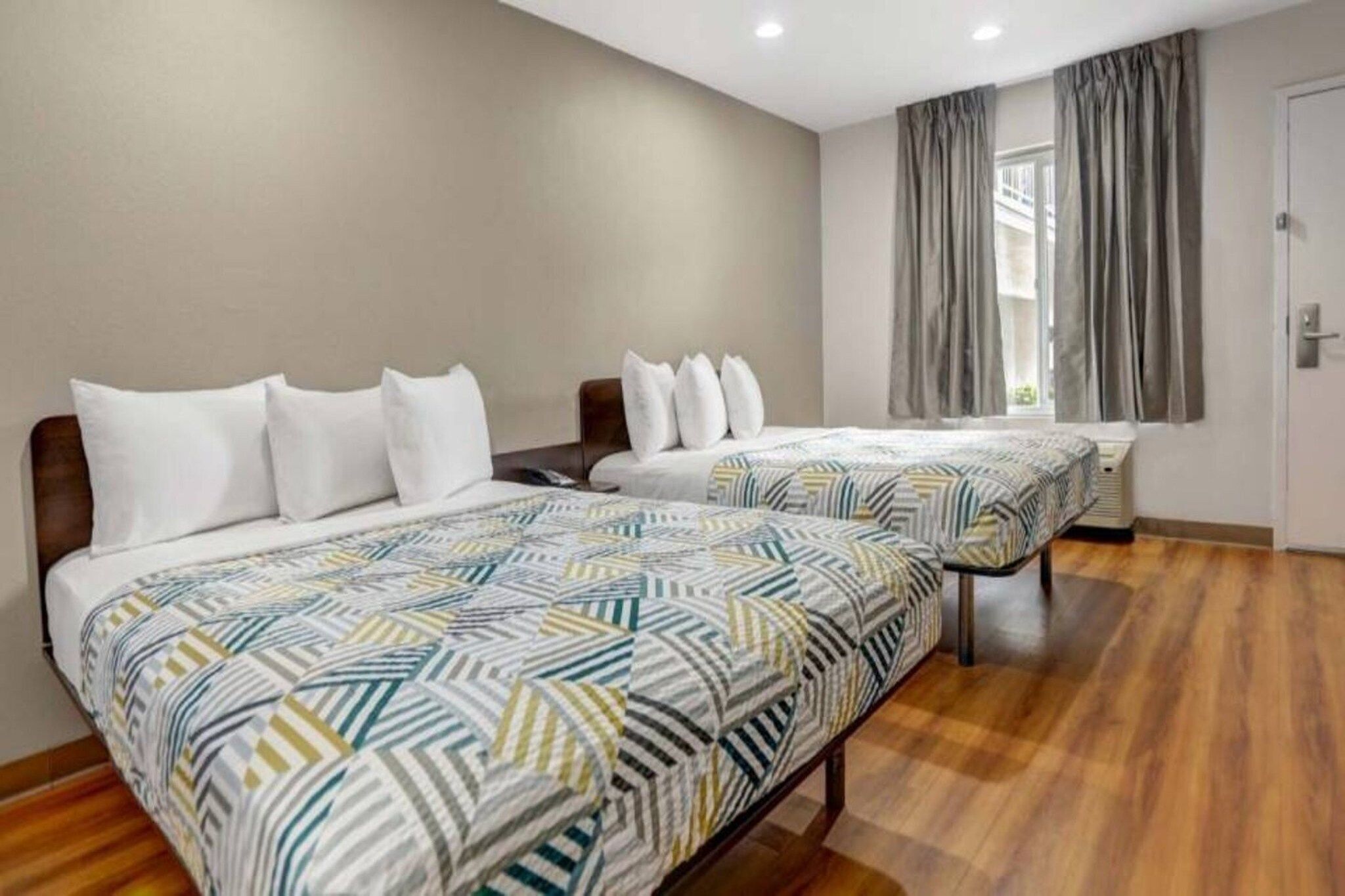 Een hotelkamer met twee bedden, een houten vloer, een raam met gordijnen en een deur.