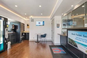 Eine moderne Hotelhalle mit einer Rezeption, einer Sitzecke und einem digitalen Bildschirm an der Wand.