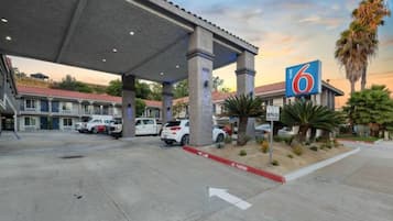 A gas station with a 6 sign, multiple cars parked, and a clear sky.