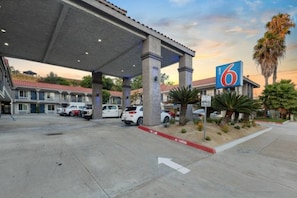 Une station-service avec une enseigne indiquant le prix de l’essence, plusieurs voitures garées et un ciel dégagé.