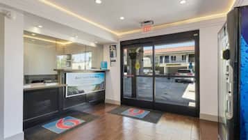 A hotel reception area with a digital screen displaying a message, a reception desk, and a glass door leading outside.
