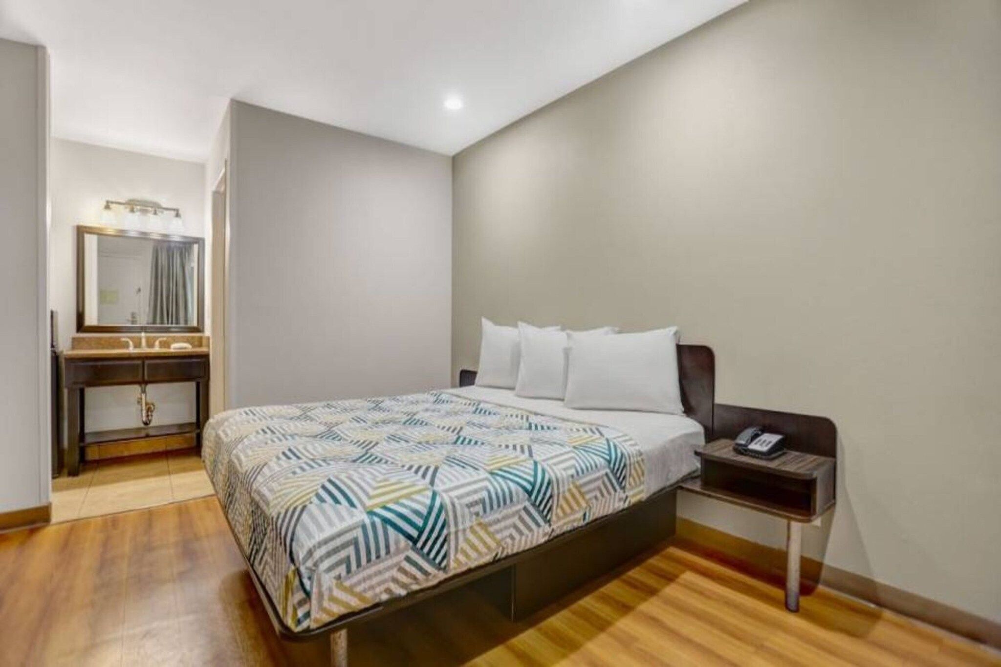 A hotel room with a bed, bedside table, and a mirror.