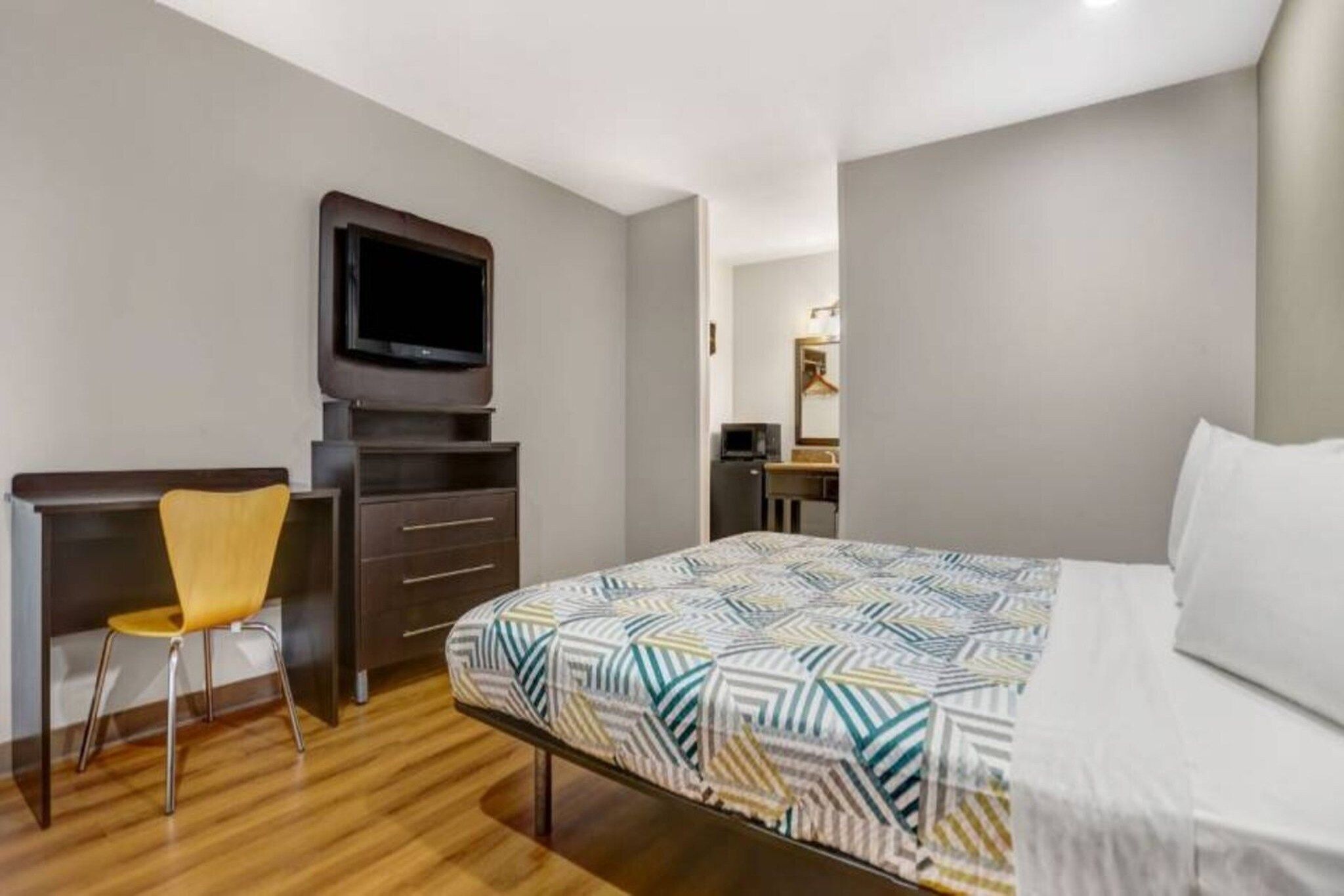 A hotel room with a bed, a desk, a chair, a television, and a mirror.