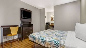 A hotel room with a bed, a desk, a chair, a television, and a mirror.