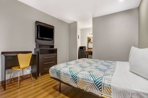 Une chambre d’hôtel équipée d’un lit, d’un bureau, d’une chaise, d’une télévision et d’un miroir.