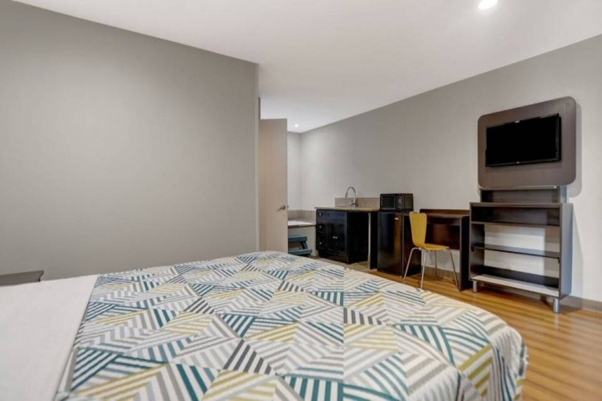 Una habitación de hotel con cama, escritorio, silla, televisor y kitchenette.