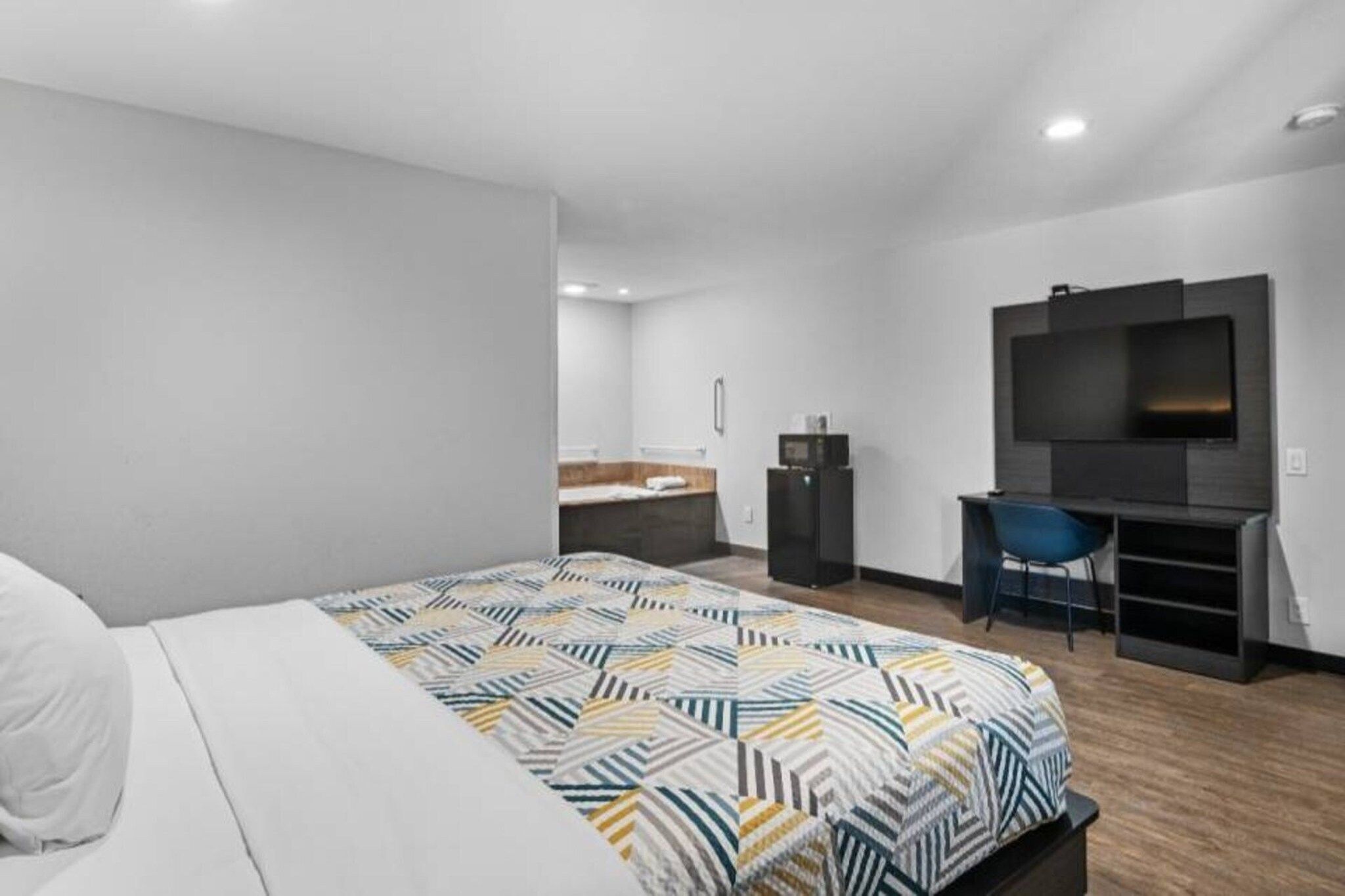 Una habitación de hotel moderna con una cama grande, un escritorio, un televisor y un baño al fondo.