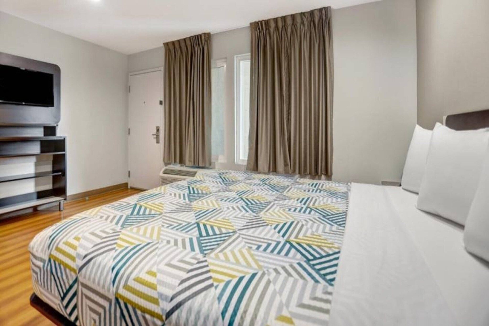 Une chambre d’hôtel avec un grand lit, un téléviseur à écran plat, un bureau avec une chaise et une fenêtre avec des rideaux.