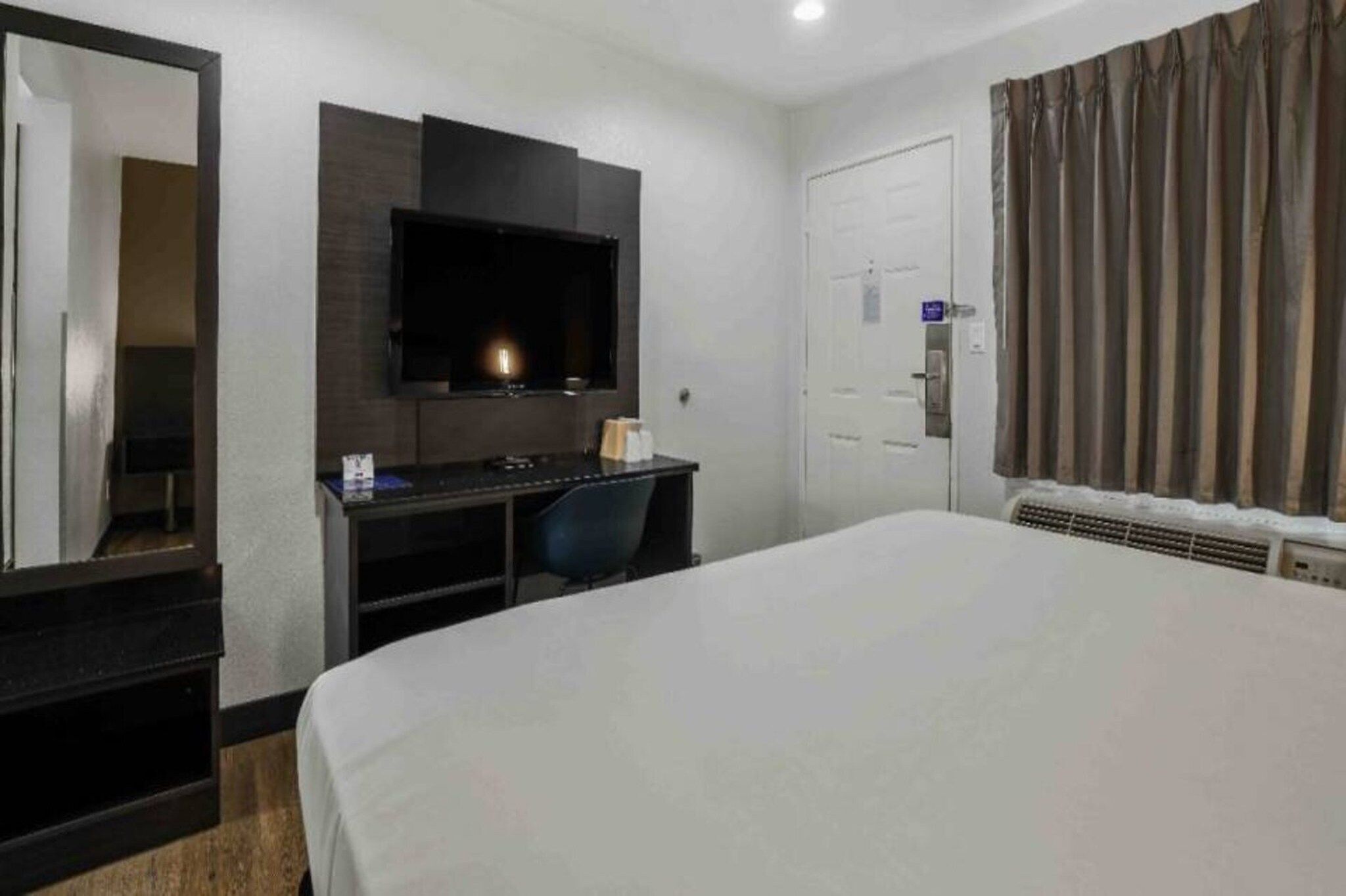 A hotel room with a bed, a desk, a TV, a mirror, a door, and curtains.