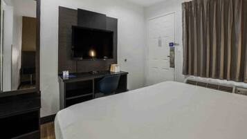 A hotel room with a bed, a desk, a TV, a mirror, a door, and curtains.
