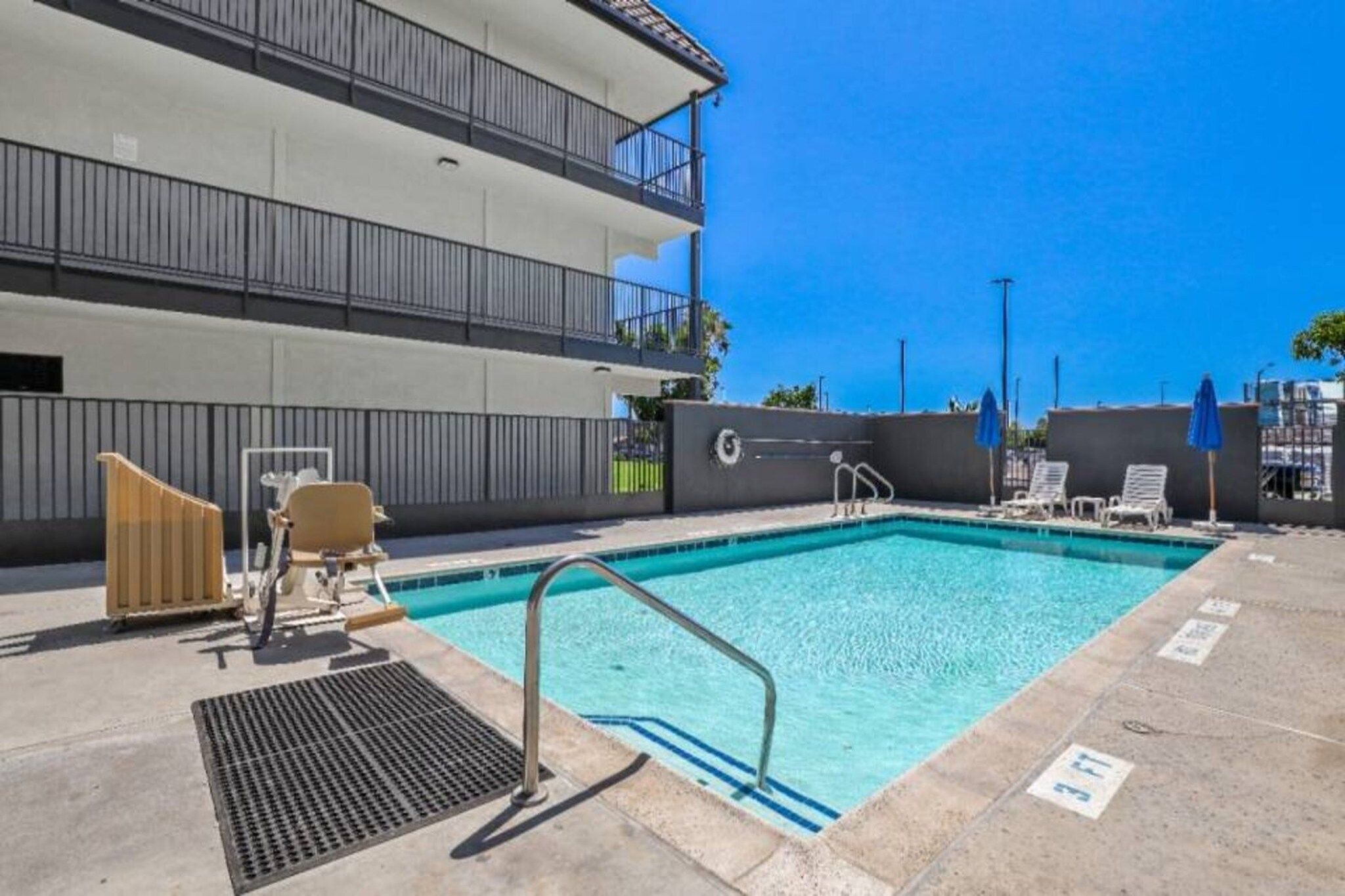 A swimming pool with a metal ladder, lounge chairs, and a building with balconies in the background.