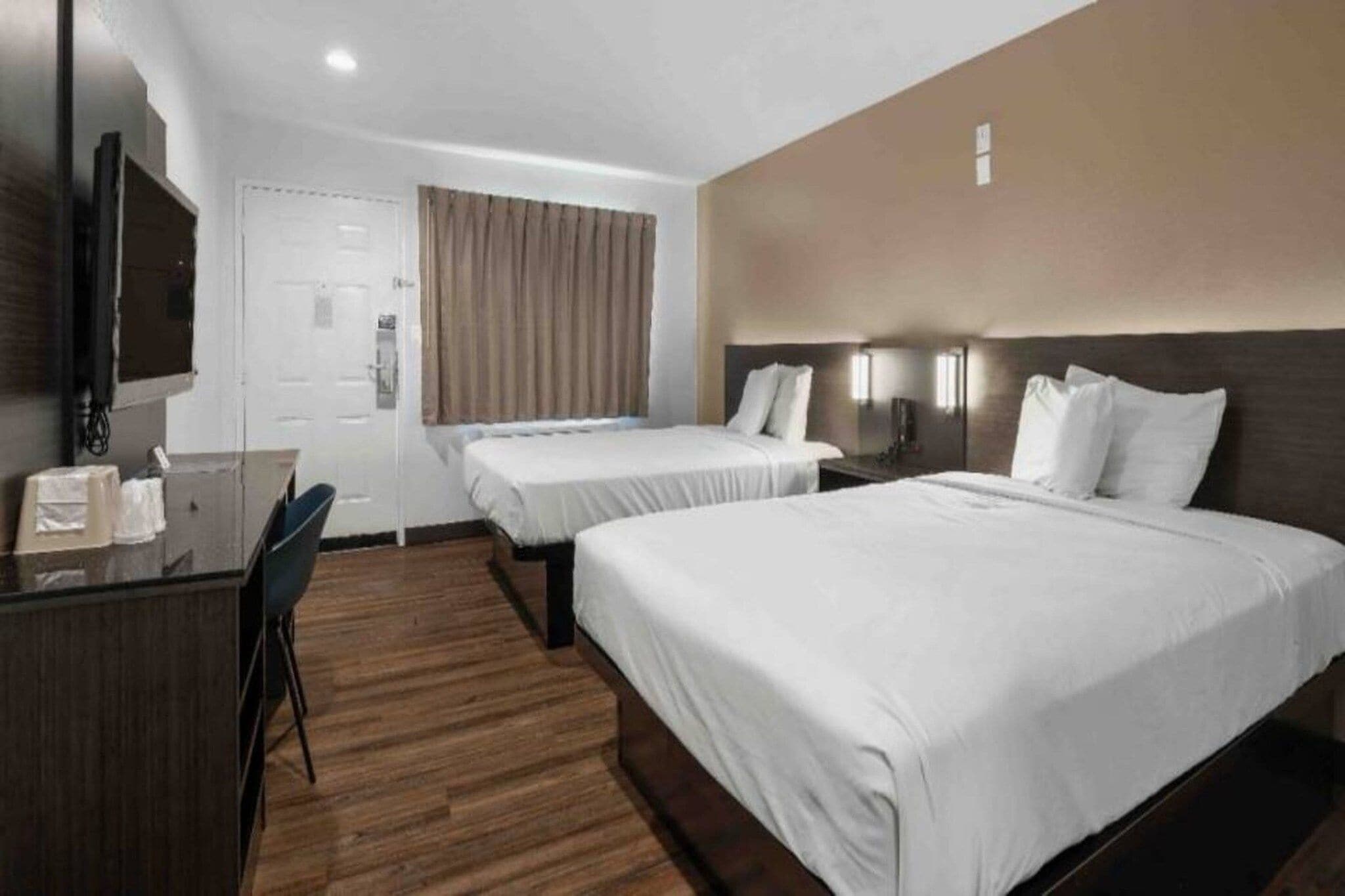 Ein Hotelzimmer mit zwei Betten, einem Schreibtisch, einem Stuhl, einem Fernseher und einer Tür.