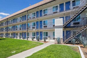 Un motel à plusieurs étages doté d’une cour centrale, avec une rangée de chambres aux portes bleues, un escalier et une pelouse bien entretenue.