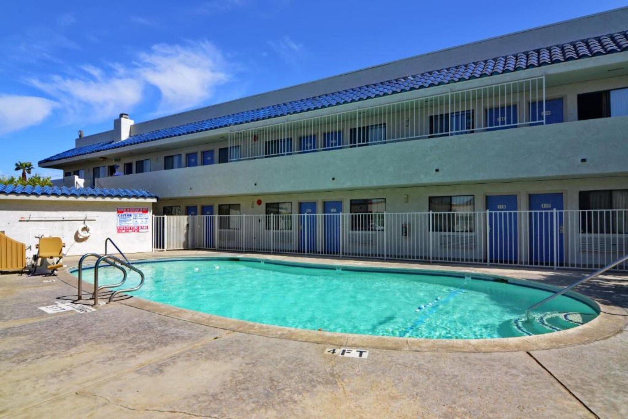 A hotel with a swimming pool, a fenced area, and a building with multiple windows and doors.