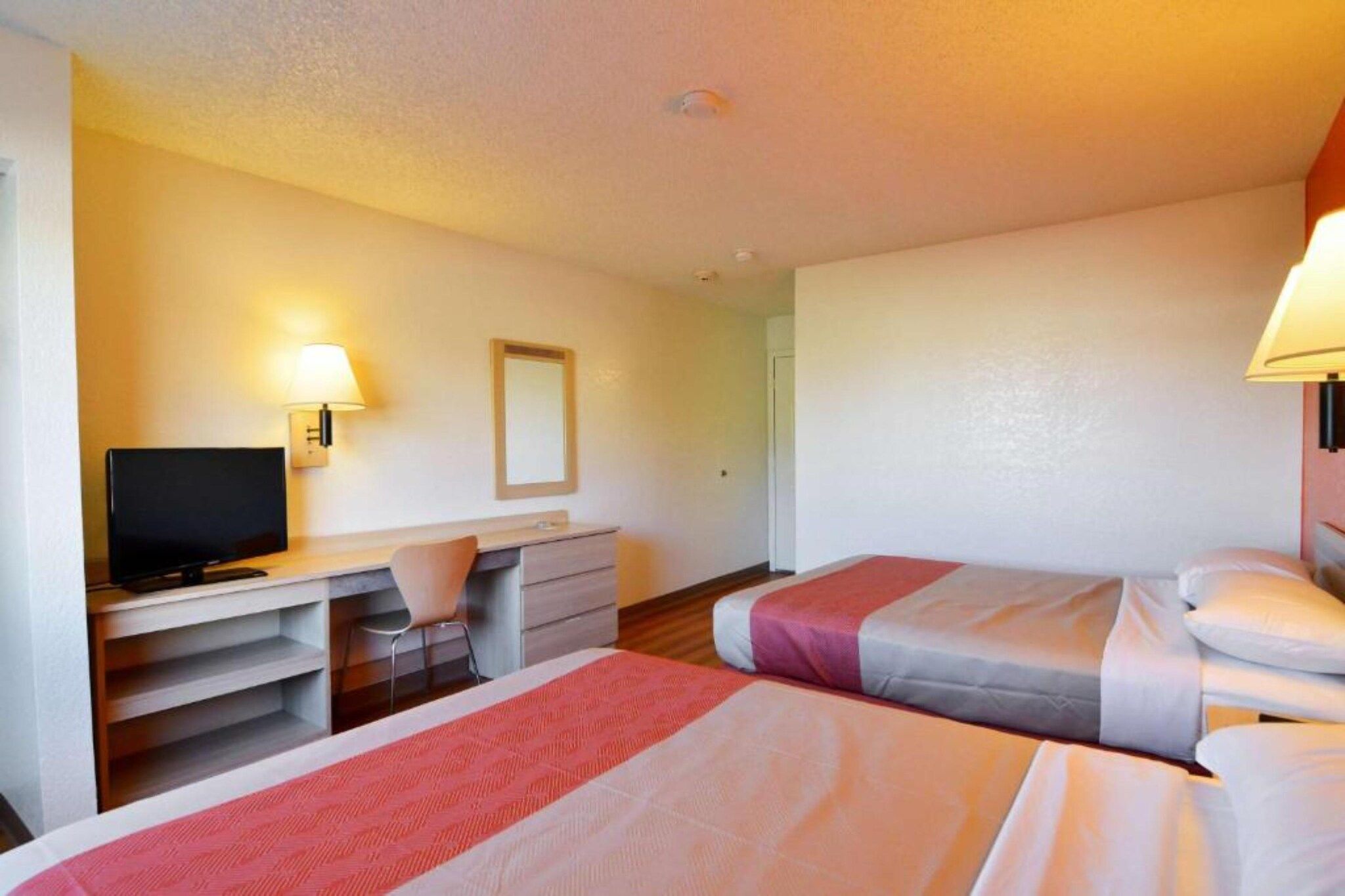 A hotel room with two beds, a desk, a chair, a television, and a mirror.