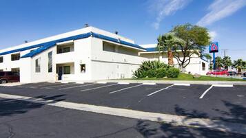 A motel with a white exterior and blue roof, a parking lot, and a '6' sign indicating the number of rooms.