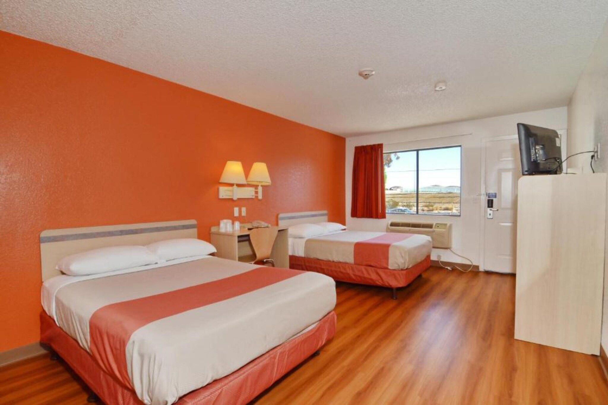 A hotel room with two beds, a desk, a chair, a TV, and a window with a view.